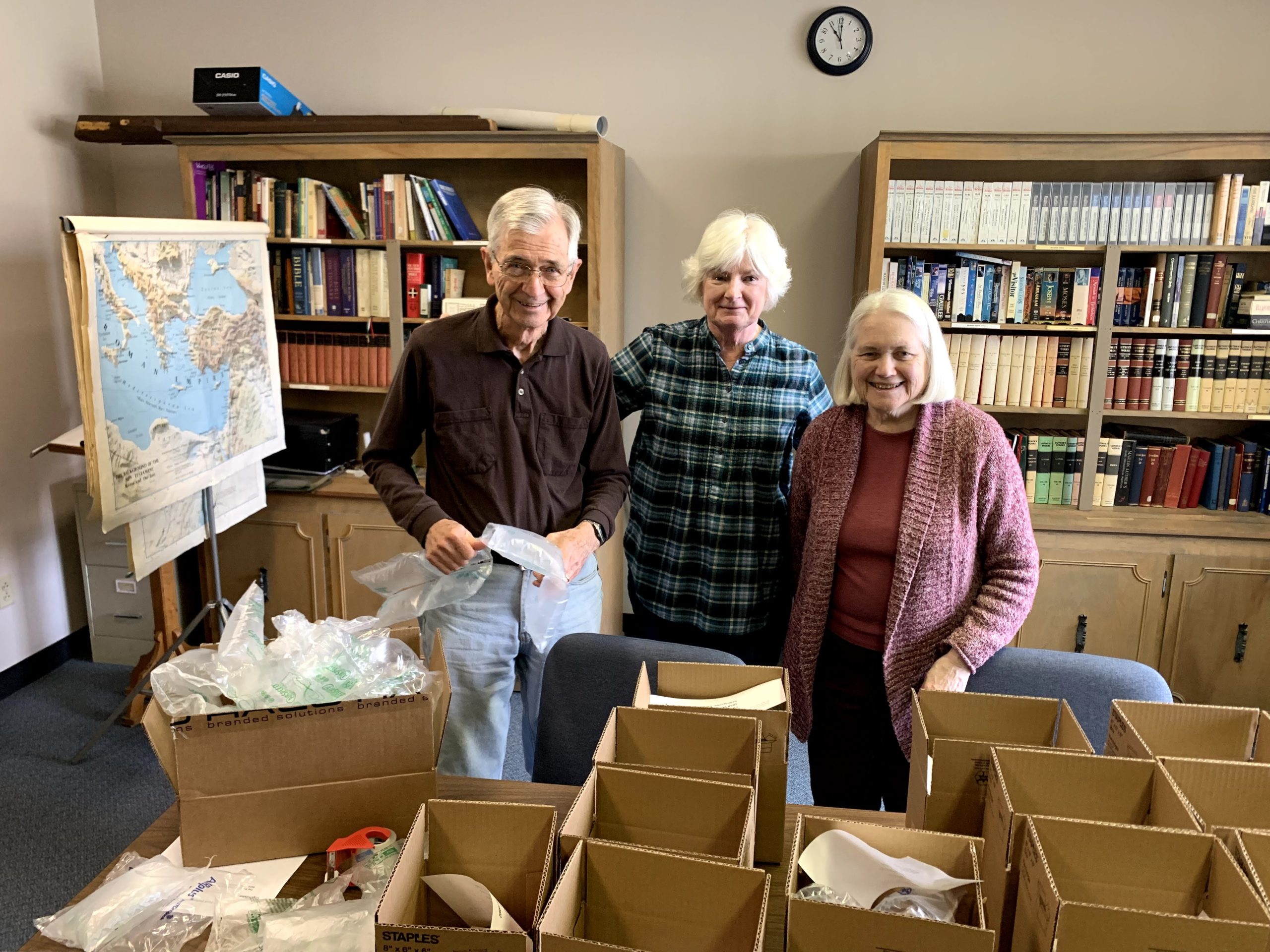 Three elderly people organizing supplies in boxes inside a library.