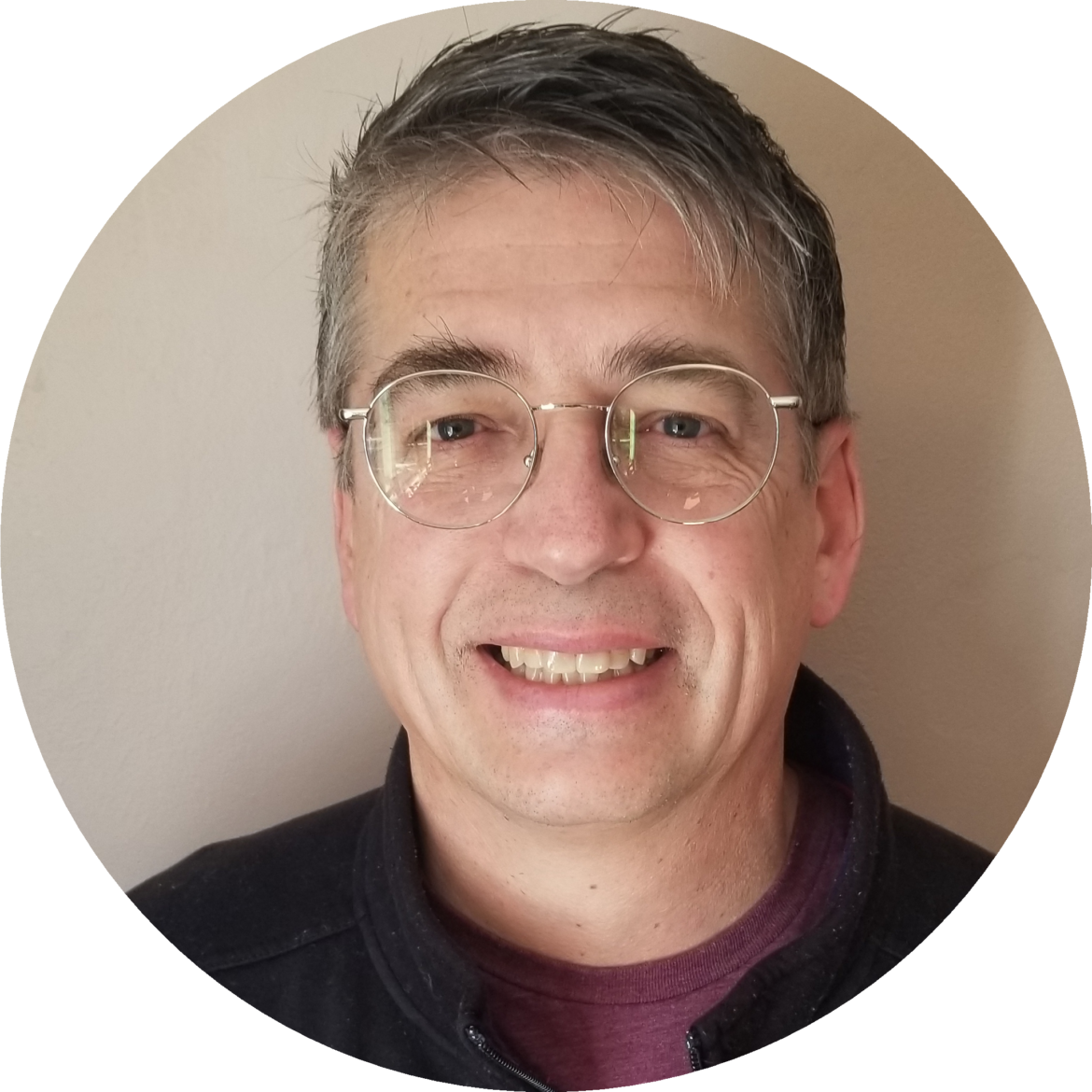 Smiling man with glasses and gray hair in a casual setting.