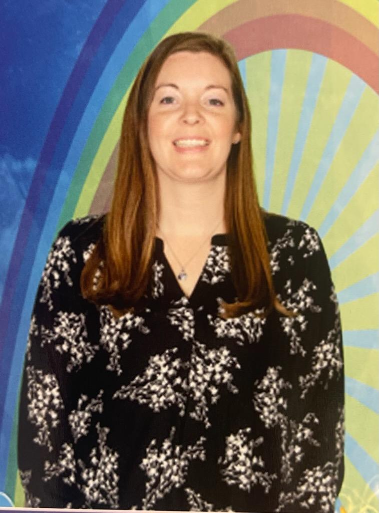 Woman with long brown hair standing in front of a colorful rainbow mural.