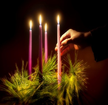 Hand lighting a candle on an Advent wreath with four candles.
