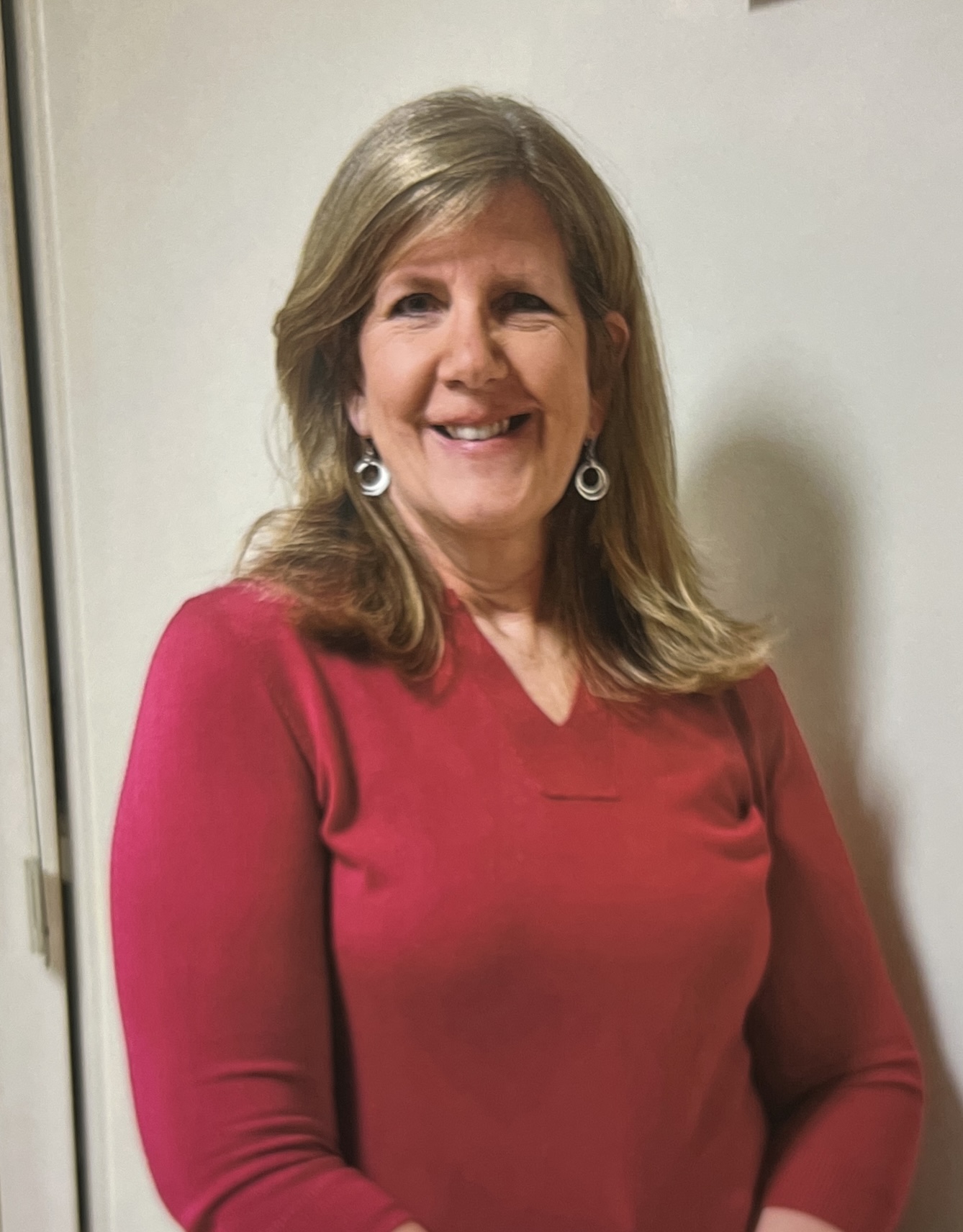 Woman in a red sweater smiling indoors.
